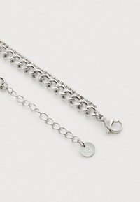 Hopeaketjua hopeasta, joka koostuu suurista litteistä lenkeistä sekä pienemmistä helmimäisistä yksityiskohdista, jossa on hummerilukko ja logokoriste.