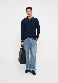 Navy long-sleeve polo shirt with green and white striped collar and cuffs, paired with light blue wide-leg jeans and a black tote bag.