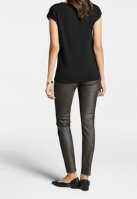 Camisa negra de manga corta con un corte relajado, combinada con pantalones ajustados de imitación cuero oscuros y brillantes, y bailarinas negras. Diseño simple, sin patrones.