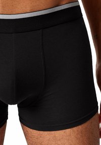 Boxer in cotone nero realizzati in tessuto liscio, con una cintura elastica grigia e una vestibilità aderente, con cuciture visibili sui lati.