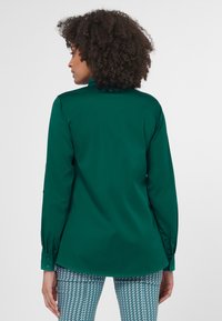 Groene langemouwen shirt met een rechte snit, knoopmanchetten en een gladde textuur, gecombineerd met gebloemde, aansluitende broek in blauw en wit.