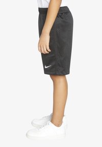 Svart mesh treningsshorts med snor i livet og hvit Nike-logo. Båret med hvite joggesko, som viser en sidevisning av antrekket.