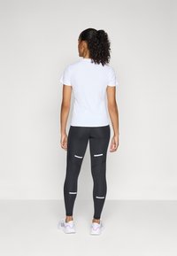 Top bianco a maniche corte, abbinato a leggings neri con accenti riflettenti. I leggings hanno un design strutturato e una texture liscia.