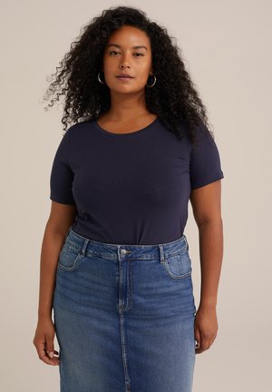 Camiseta de algodón color azul marino con cuello redondo, combinada con una falda de mezclilla de cintura alta que presenta un botón en la parte frontal y bolsillos.