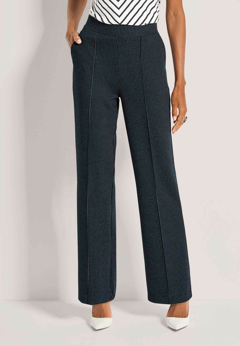 Weit geschnittene, gestreifte Hose in Dunkelblau mit strukturierter Stoffqualität, seitlichen Taschen und einem glatten Bund. Kombiniert mit weißen High Heels.