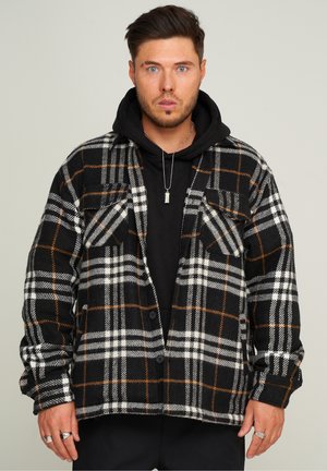 Schwarzes und weißes karriertes Flanellhemd mit orangefarbenen Akzenten, zwei Brusttaschen und einem Knopfverschluss, über einem schwarzen Hoodie getragen.