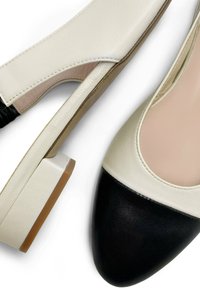 Zapatos de tacón bloque en tonos beige y negro, con punta afilada, que presentan una parte superior de cuero liso y un detalle de bloque de color en contraste.