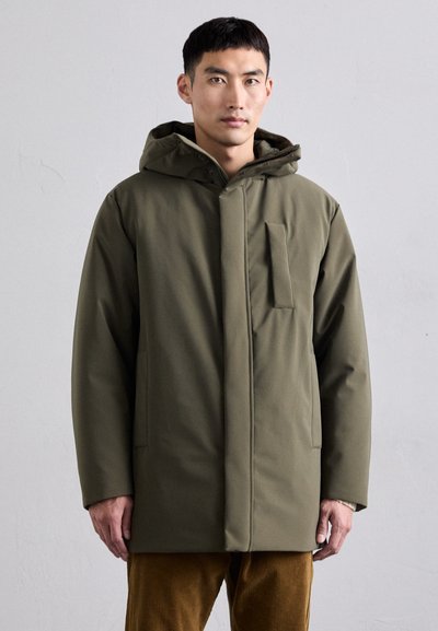 Manteau isolé vert olive avec capuche, présentant une fermeture à l'avant et une poche poitrine. Texture lisse et forme moderne et rectangulaire.