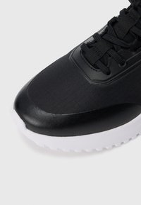 Μαύρο αθλητικό παπούτσι με λείο συνθετικό πάνω μέρος, υφασμάτινες υφές και λευκή καουτσούκ σόλα με αυλάκια πρόσφυσης.