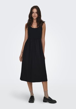 Sort ærmeløs kjole med en ribbet bodice og en fuld, flydende nederdel. Båret med sorte loafers og teksturerede, mønstrede strømper.