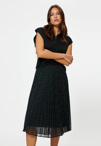 Sort top med korte ærmer, parret med en plisseret sort nederdel med hvide polka dots, hvilket skaber en lagdelt tekstur og design.