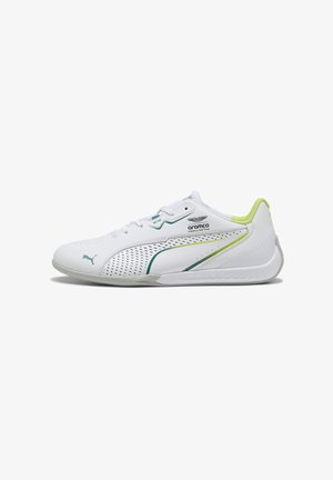 Zapatilla deportiva blanca con parte superior perforada, acentos en verde y azul, talón texturizado y suela de goma. Presenta el logo de Puma y detalles de la marca.