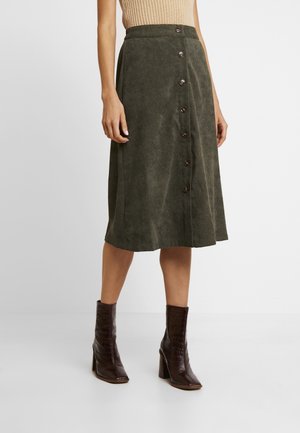 Jupe vert olive en tissu doux, forme A-line, dotée d'une fermeture à boutons sur le devant avec des boutons marron foncé. Associée à des bottes à talons marron.