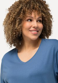 Blaues V-Ausschnitt-T-Shirt aus weichem Baumwollstoff. Hat kurze Ärmel und eine glatte Textur. Zeigt eine Nahaufnahme des Oberkörpers und des Gesichts eines Modells.
