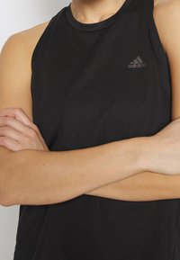 Camiseta de tirantes negra de entrenamiento con una tela texturizada, diseño sin mangas y un pequeño logo negro de adidas en el pecho.