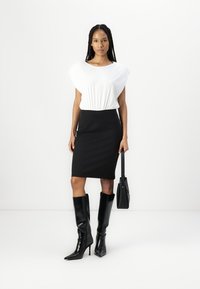 Haut blanc à manches courtes avec taille froncée, associé à une jupe crayon noire ajustée. Bottes noires à talons aiguilles montantes jusqu'au genou et un petit sac à main.