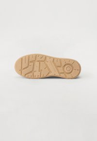 Semelle de chaussure en caoutchouc brun avec texture à motifs, présentant des rainures et un logo circulaire. Surface lisse avec bords renforcés pour la stabilité.
