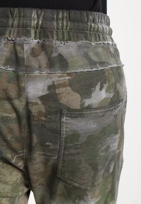 Camo-muster Jogginghosen in Grün- und Brauntönen, mit einem strukturierten Bündchen und einer Gesäßtasche sowie einem ausgefransten Saum.