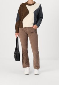 Stickad tröja med ett mönster i brunt, kräm och marinblått; matchad med beige byxor i kordfløyel och vita sneakers; håller en svart handväska.