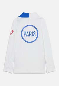 Chemise blanche à manches longues avec un col bleu, grand texte "PARIS" bleu à l'intérieur d'un cercle pointillé dans le dos, accent rouge sur la manche.