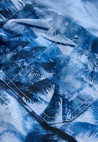 Tela azul con un patrón de palmeras en varios tonos de azul. Incluye detalles de costura visibles a lo largo de los bordes.