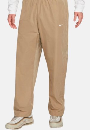 Light beige Nike pants with a loose fit, elastic waistband, and subtle logo. Made from smooth, water-resistant material.