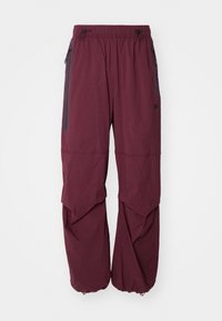 Bordeaux buitenbroek van lichtgewicht stof, met een elastische tailleband, ritszakken en een uniek gelaagd ontwerp.