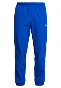 Blå vindjacka byxor med elastisk midja, avsmalnande ärmslut och vita sidostrecker. Tillverkade av ett lätt, glattyg. Logotyp på framsidan.