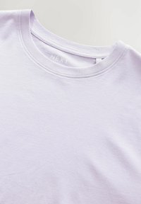 Camiseta de algodón de color púrpura claro con cuello redondo, que presenta una textura suave y un sutil logo en relieve en el cuello.