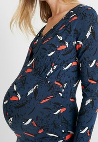 Mammaklänning med en marinblå bas och abstrakta mönster i rött, vitt och svart. V-ringad design och figursydd silhuett, som rymmer en gravidmage.