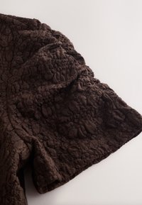Dark brown fabric with raised floral pattern, soft texture, and subtle folds on a light surface.