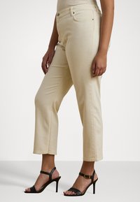 Beige høyhåndte jeans med rett benkutt, med en subtil tekstur og frontlommer, sammen med svarte strappy høyhælte sandaler.