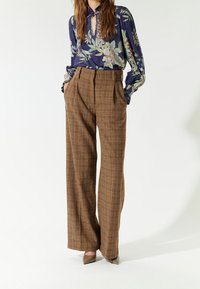 Blouse bleu marine à motif floral avec un décolleté en goutte d'eau ; pantalon à carreaux marron taille haute et jambes larges ; tissu lisse et coupe ajustée.