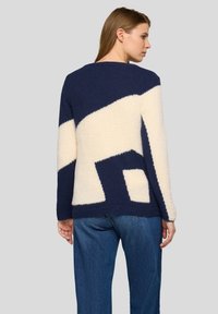 Marineblaue und cremefarbene Pullover mit geometrischem Muster und weicher, strukturierter Oberfläche. Verfügt über einen Rundhalsausschnitt und lange Ärmel.