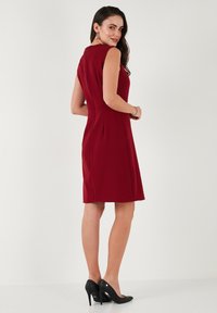 Bordo halter haljina s tijesnim siluetom, krojena do koljena, od glatkog materijala, s suptilnim šavovima, uparenim s crnim visokim petama.