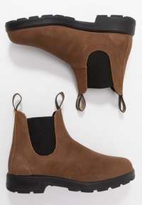 Botas de ante marrón hasta el tobillo con paneles laterales elásticos, lengüetas y una suela de goma negra con un patrón de textura en la banda de rodadura.