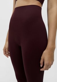 Leggings bordeaux à côtes avec une taille haute, présentant une texture lisse et un design ajusté, s'étendant jusqu'au mi-botte.