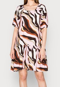Mujer con un vestido hasta la rodilla con mangas cortas abullonadas y un patrón abstracto en tonos de rosa, marrón, beige, naranja y blanco.