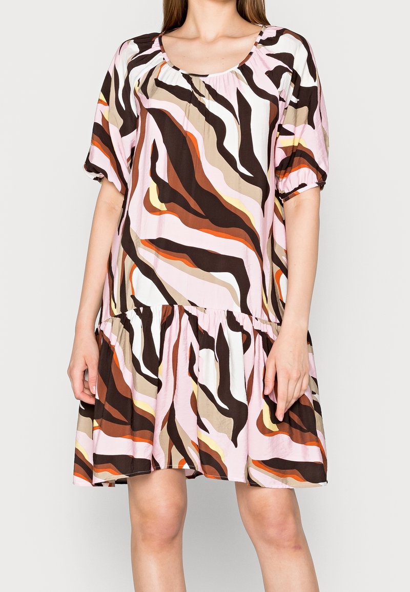 Mujer con un vestido hasta la rodilla con mangas cortas abullonadas y un patrón abstracto en tonos de rosa, marrón, beige, naranja y blanco.