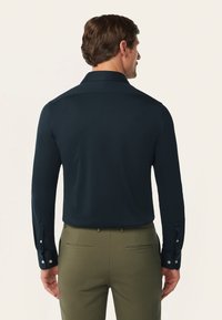 Navyblauwe overhemd met lange mouwen, een gestructureerde kraag, een op maat gemaakte pasvorm en knoopmanchetten, gecombineerd met olijfgroene broeken met achterzakken.