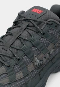 Nike sneaker in dark gray with textured fabric, grid pattern, rubber accents, and red logo. Features lacing system and padded collar.