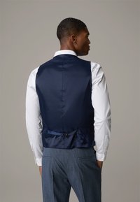 Navy satijnen vest met een gladde textuur, een op maat gemaakte pasvorm en een verstelbare rugband. Gecombineerd met een wit overhemd en grijze patroonbroek.