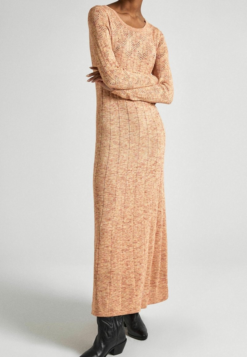 Lång stickad klänning i mjuka orange toner, med en ribbad struktur och rund halsringning, tillsammans med svarta ankelstövlar.