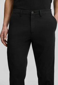 Schwarze Hose aus glattem Stoff mit flacher Vorderseite, Knopfschluss, Gürtelschlaufen und Seitentaschen. Figurumspielender Schnitt mit einem eleganten Design.