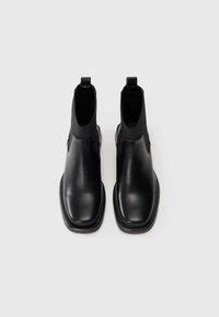 Czarne skórzane buty chelsea z elastycznymi panelami bocznymi, gładką teksturą, okrągłym noskiem i niskim obcasem w stylu klocka. Minimalistyczny design, brak widocznej marki.