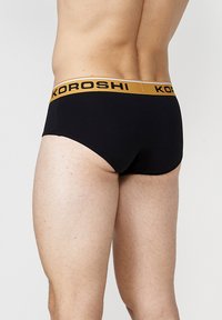 Schwarze Baumwollunterhose mit einem goldenen elastischen Bund, auf dem der Markenname "KOROSHI" steht. Sie verfügt über eine enge Passform und eine glatte Textur.