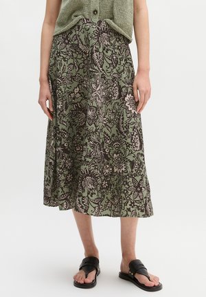 Zielona kwiatowa spódnica midi noszona z zielonym bezrękawnikiem i czarnymi sandałami, widok z przodu od talii do stóp na neutralnym tle.