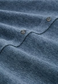 Marineblauwe stof met een zachte textuur, met een zichtbare knop en subtiele golfpatronen, die een gladde, gelaagde uitstraling toont.