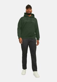 Mørkegrøn hoodie med frontlomme og snørebånd, parret med sorte cargo-bukser med sidelommer og hvide sneakers.