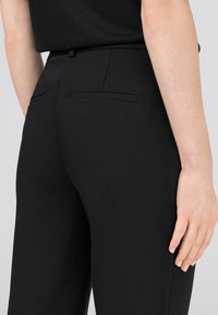 Svarta skräddarsydda byxor med en mjuk textur, som har två bakfickor och en ren midjebandsdesign. Tyget är matt och strukturerat.